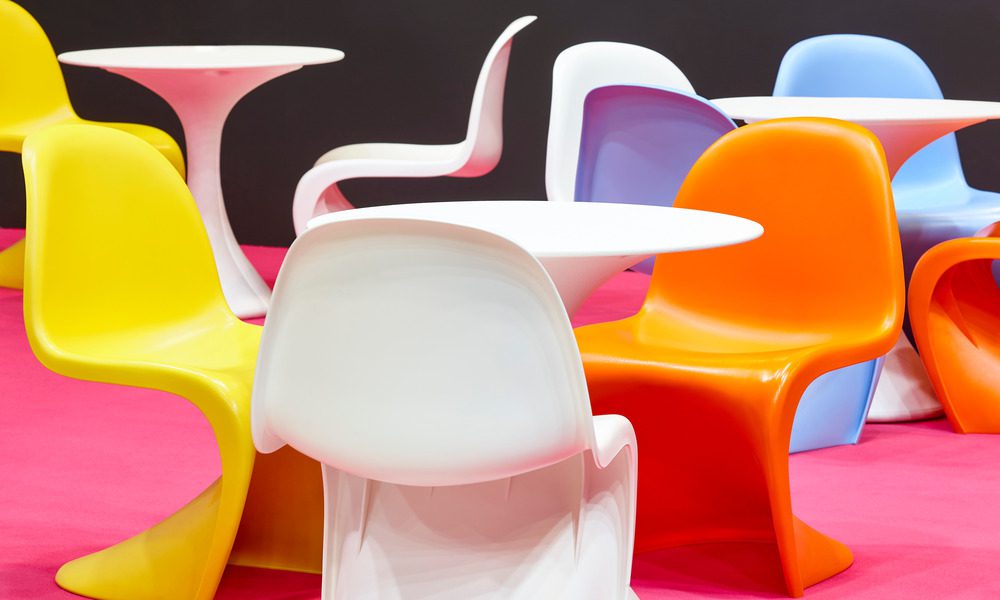 Several chairs of different colors with a contemporary design made of plastic sit around white plastic tables.