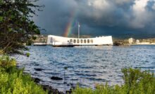 A beautiful rainbow behind the USS Arizona located at Pearl Harbor. The sky is dark and cloudy around the rainbow.