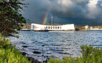A beautiful rainbow behind the USS Arizona located at Pearl Harbor. The sky is dark and cloudy around the rainbow.