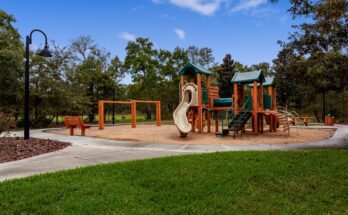 An outdoor playground on a clear day with a cement path, grass on one side and engineered wood fibers on the other.