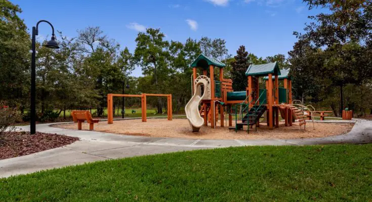 An outdoor playground on a clear day with a cement path, grass on one side and engineered wood fibers on the other.