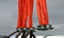 Multiple industrial cable slings are covered in a bright orange protective material. The slings hang together.