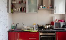 A kitchen with red and silver cabinets. The cabinet doors are open and there is clutter on the counters.