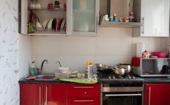A kitchen with red and silver cabinets. The cabinet doors are open and there is clutter on the counters.