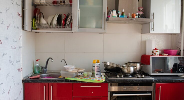 A kitchen with red and silver cabinets. The cabinet doors are open and there is clutter on the counters.