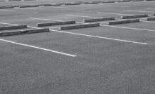 An empty parking lot with grey asphalt, parking blocks in each spot, and white paint defining each space.