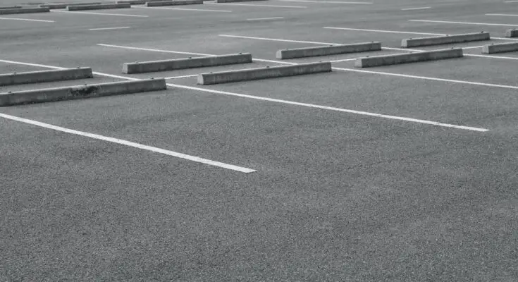 An empty parking lot with grey asphalt, parking blocks in each spot, and white paint defining each space.