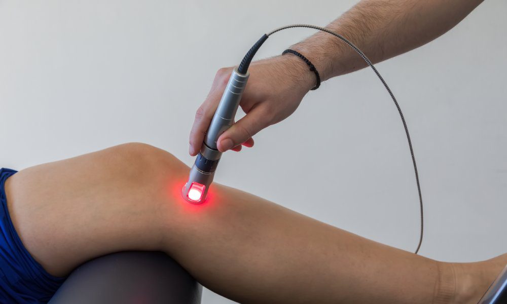 A close-up of a doctor focusing red laser light on a spot just below the bent knee of a patient.