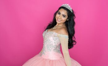 A teenage girl poses in a beautiful pink dress, wearing a tiara. The dress has a poofy skirt with an embellished top.