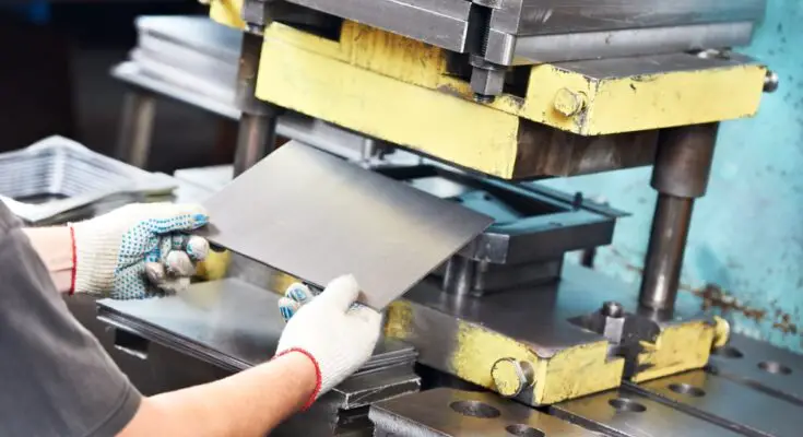 A team member wearing white protective gloves puts a small piece of sheet metal into a yellow sheet metal machine.