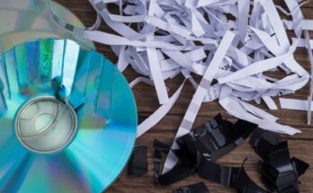 A close-up view shows a partially shredded CD, shredded paper, and shredded black paper on a wooden surface.
