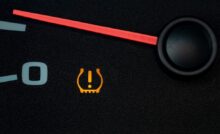 A close-up view shows a yellow U-shaped symbol with an exclamation point in the center lit up on a vehicle dashboard.