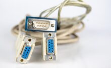 A collection of RS232 connections with blue ports and off-white cables sitting on a white surface.