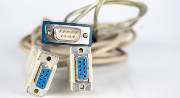 A collection of RS232 connections with blue ports and off-white cables sitting on a white surface.