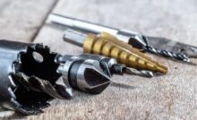 A selection of drill bits featuring different shapes, styles, and materials. They are resting in a row on a wooden surface.