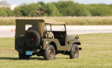 A vintage World War II era Willys Jeep parked in the middle of a large field. The Jeep is dark green in color.