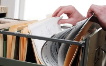 A close-up view of a person's hand flipping through a pile of neatly organized files and folders inside a drawer.