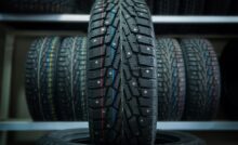 A car tire has red, blue, and white dotted lines on it. More tires with colored lines are behind it on a shelf.