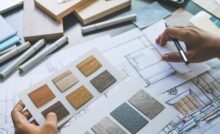A person holds interior design sketches and material and color samples in one hand and a pencil in the other hand.
