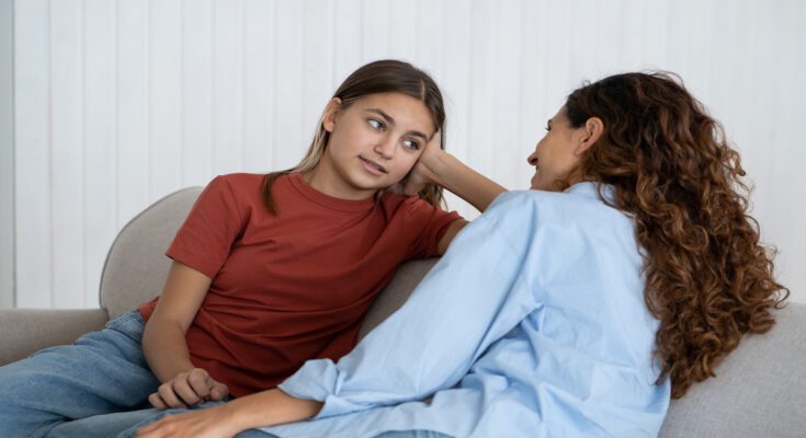 A mother and her pre-teen child sitting on a couch together and face each other as they have a discussion.