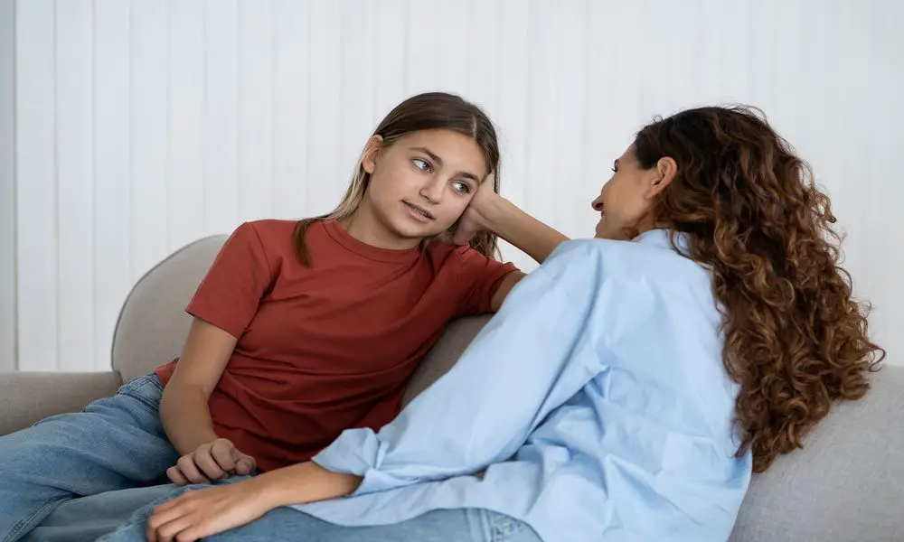 A mother and her pre-teen child sitting on a couch together and face each other as they have a discussion.
