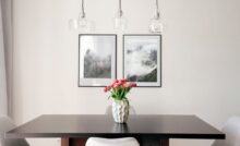 A minimalist, modern dining area with a white vase holding pink flowers as a centerpiece on the table.