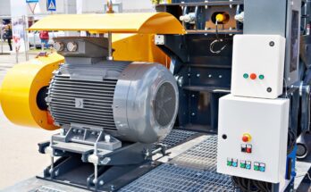 A large electric motor located outdoors with a control panel next to it. The panel has a few buttons on it.