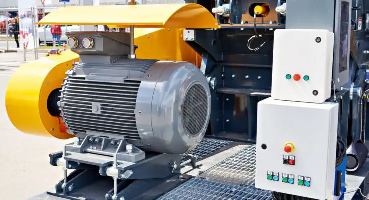 A large electric motor located outdoors with a control panel next to it. The panel has a few buttons on it.