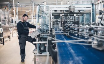 A person operating a touchscreen panel next to an automated conveyor line in a large bottling plant.