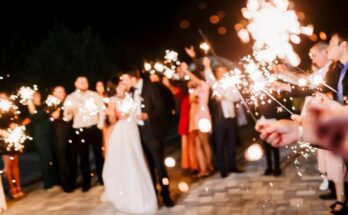 At a wedding, the bride and groom kiss while all of the other people around them hold out bright sparklers.