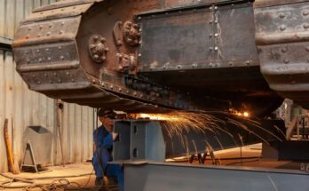 An industrial worker grinds on an old armored tank in a factory workshop. Sparks are flying off the metal.