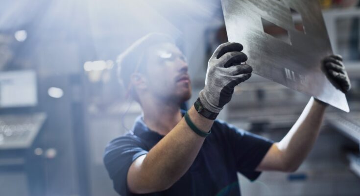 A worker examining piece in steel factory. They're wearing protective gloves while holding the fresh piece of metal.
