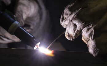 An extreme close-up shot of gloved hands using TIG (tungsten inert gas) welding, emitting a bright white light.