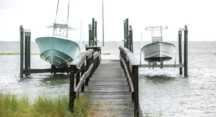 A small wooden boat dock with a long ramp leading to two boats. Both boats are elevated over the water.