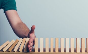 A person holding their hand in the way of a series of falling wooden blocks to protect other standing blocks.