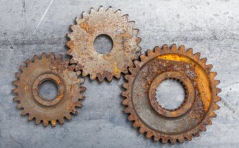 Three rusted metal gears of different sizes sit interlocked with each other on a gray concrete floor.