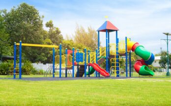 A colorful playground contains a twisty slide, monkey bars, stairs, and two straight slides. It sits on gray surfacing.