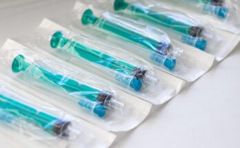 A close-up view shows several blue and teal syringes inside medical-grade packaging. They line up in a row.