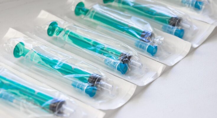 A close-up view shows several blue and teal syringes inside medical-grade packaging. They line up in a row.