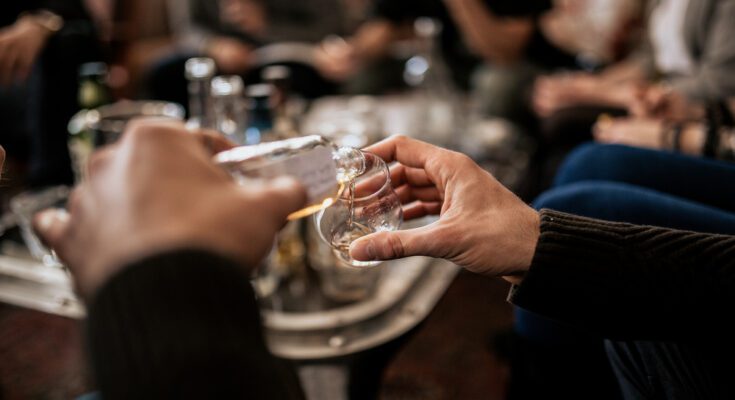 A close-up of a man's hand holding and pouring whisky from a fine alcohol sample of Japanese whisky.