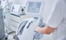 A person wearing personal protective gear grabs a part of a medical device in a room filled with other equipment.