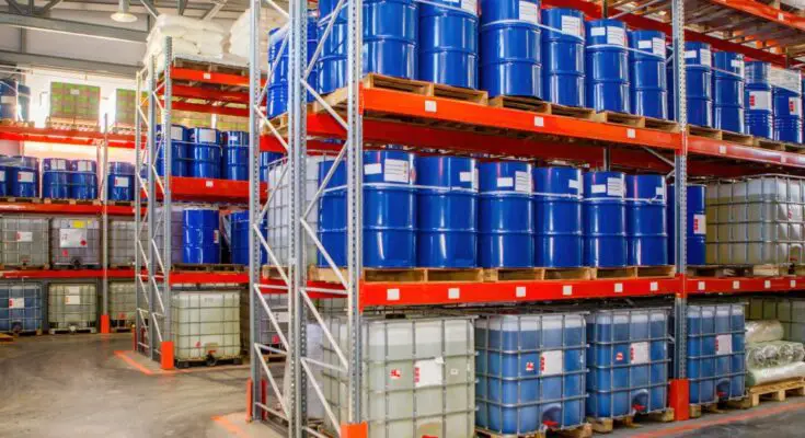 Warehouse racks stacked with blue chemical storage barrels. They sit on pallets in the storage racks.