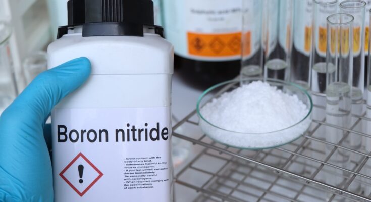A person in a blue latex glove holds a white bottle labeled "boron nitride" near their workstation with vials.