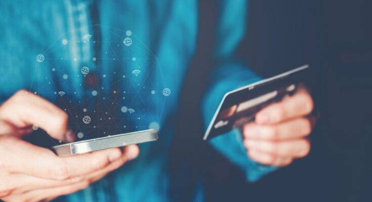 Someone in a button-up shirt holding a smartphone and credit card. There are a bunch of internet graphics popping off the phone.