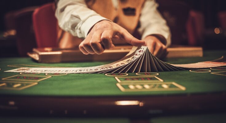 A close-up of a casino dealer at the gambling table. The dealer is shuffling cards in a line, stacked on top of each other.