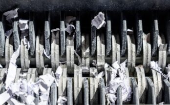 A close-up of the blades of a paper shredder. There are tiny pieces of paper stuck between the blades.