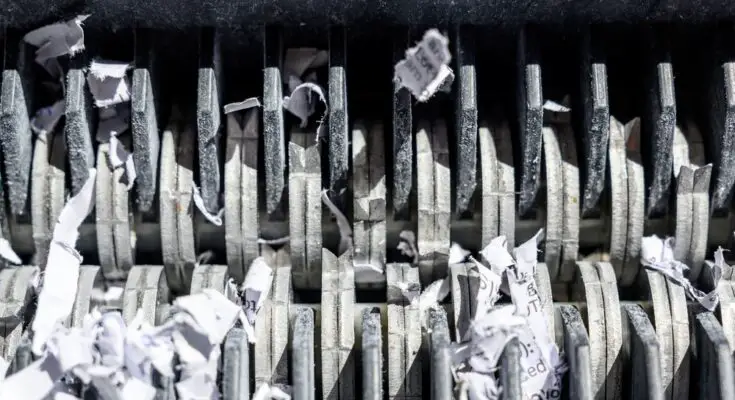 A close-up of the blades of a paper shredder. There are tiny pieces of paper stuck between the blades.