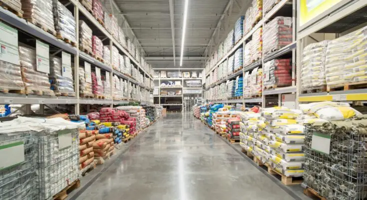 A warehouse aisle with shelves stocked with supplies, all placed on wooden pallets on both the floor and the shelving.