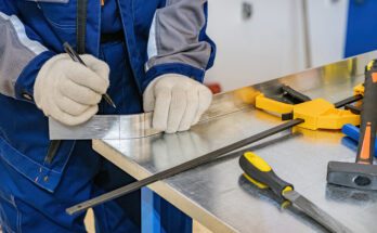 A metalworker marking a piece of metal with a marker. There are multiple measuring tools next to his workspace.