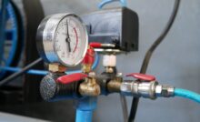 A close-up of a mechanical gauge on a compressed air system with blue pipes, blue tubes, and brass and silver fittings.